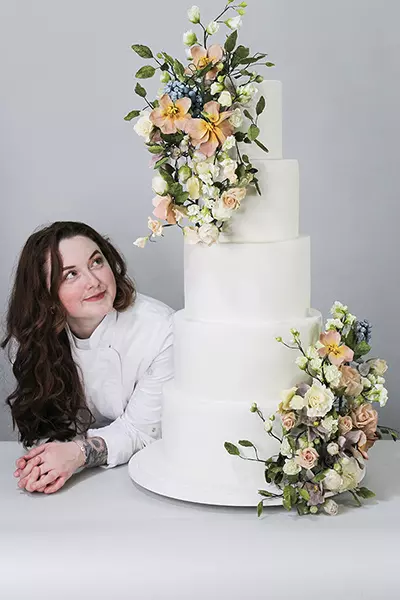 Jordan Ellen looking at her own white five-tiered wedding cake