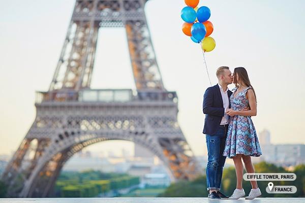 Loving couple with bunch of colorful balloons kissing near the Eiffel tower in Paris, France