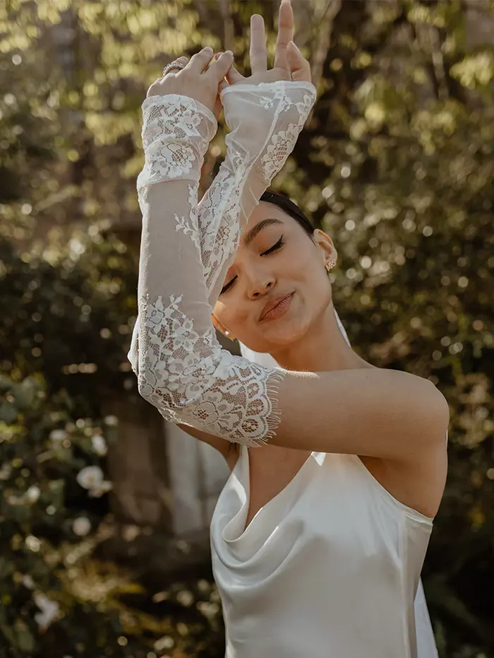 model in wedding dress wearing white lace bridal gloves with arms crossed over in the air