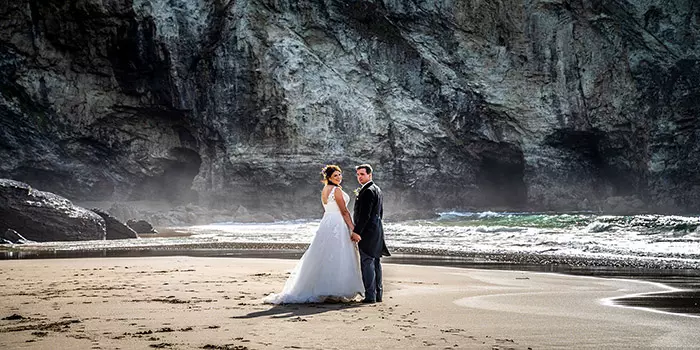 Bride and Groom holding hands turning to face photographer on beach, Trebarwith Strand, North Cornwall, United Kingdom