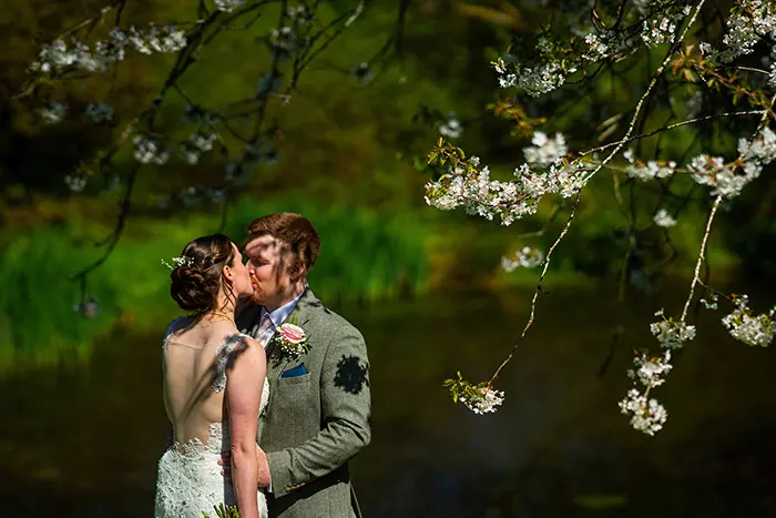 Bride and groom kissing under cherry tree blossom at The Green, Upton Cross, Cornwall, United Kingdom